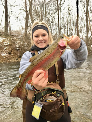 Maddie holding a rainbow trout in river.
